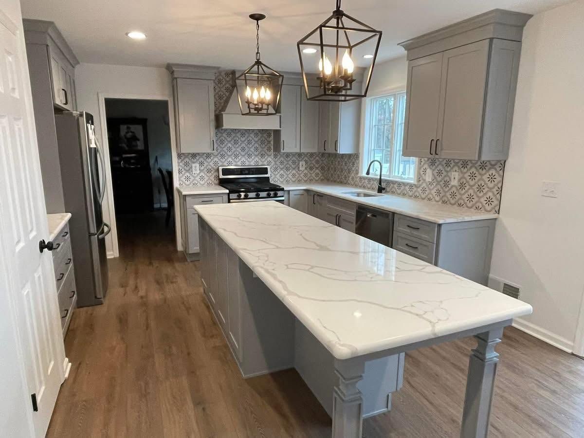 Modern kitchen with white island, gray cabinets, wood floors, and pendant lights