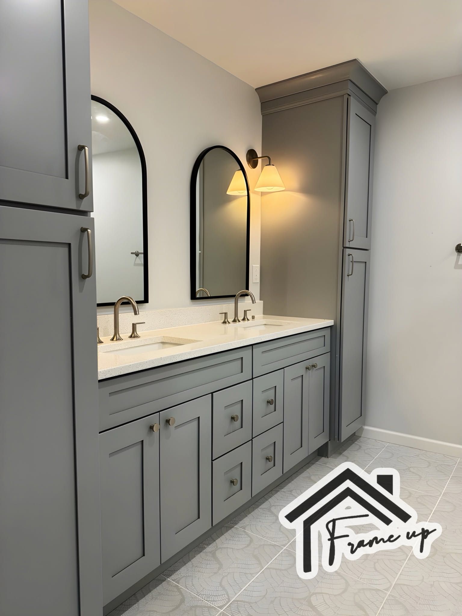 Gray double-sink bathroom vanity with arched mirrors, brass sconces, and white countertops.