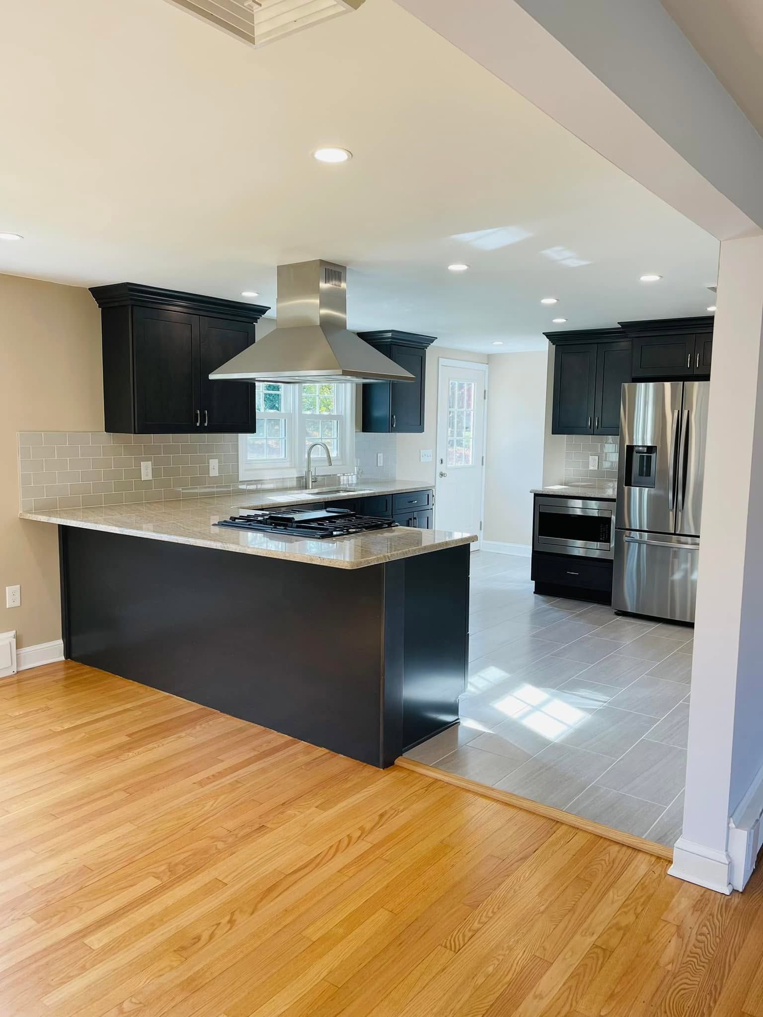 Bright kitchen with dark cabinets, stainless steel appliances, a breakfast bar, and hardwood flooring.
