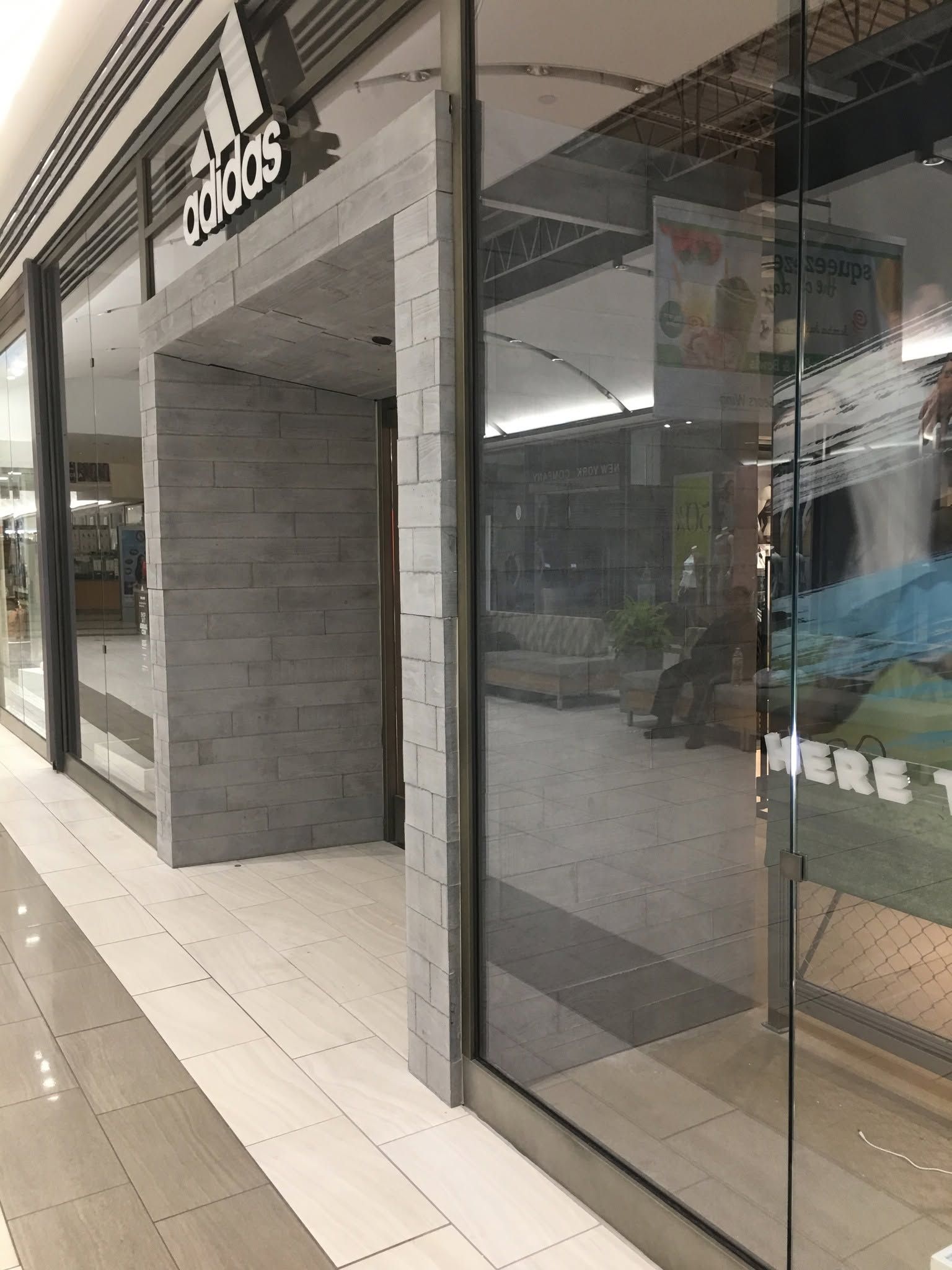 Storefront with large glass windows, tiled sidewalk, and a gray stone entrance facade.