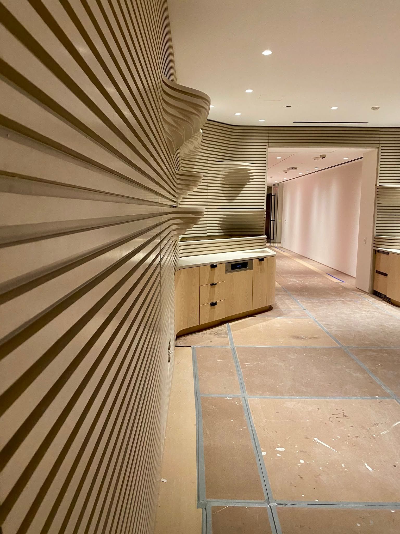 Modern interior hallway with a striped wall, wood cabinet, and curtained opening under recessed lights