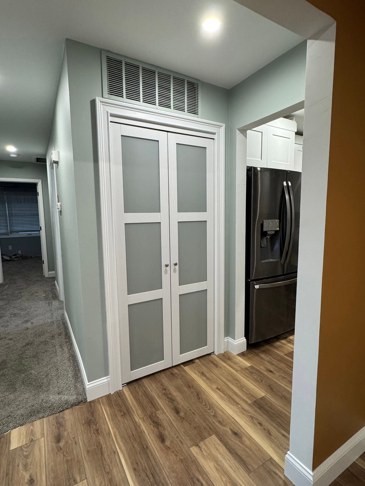 Hallway with white double doors, wood flooring, gray walls, and a stainless steel refrigerator nearby
