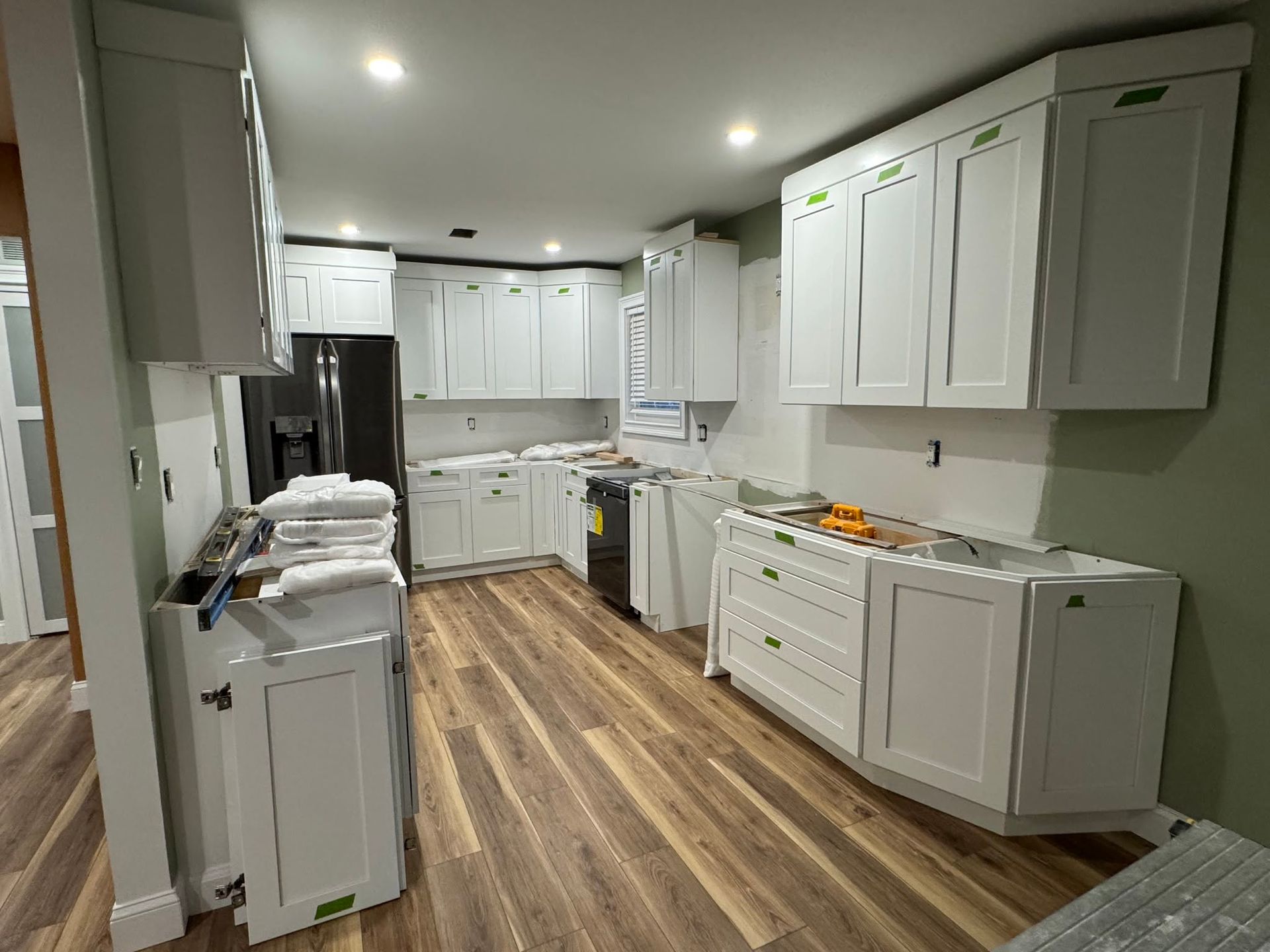 Modern white kitchen with wood floors, stainless fridge, and bright recessed lighting