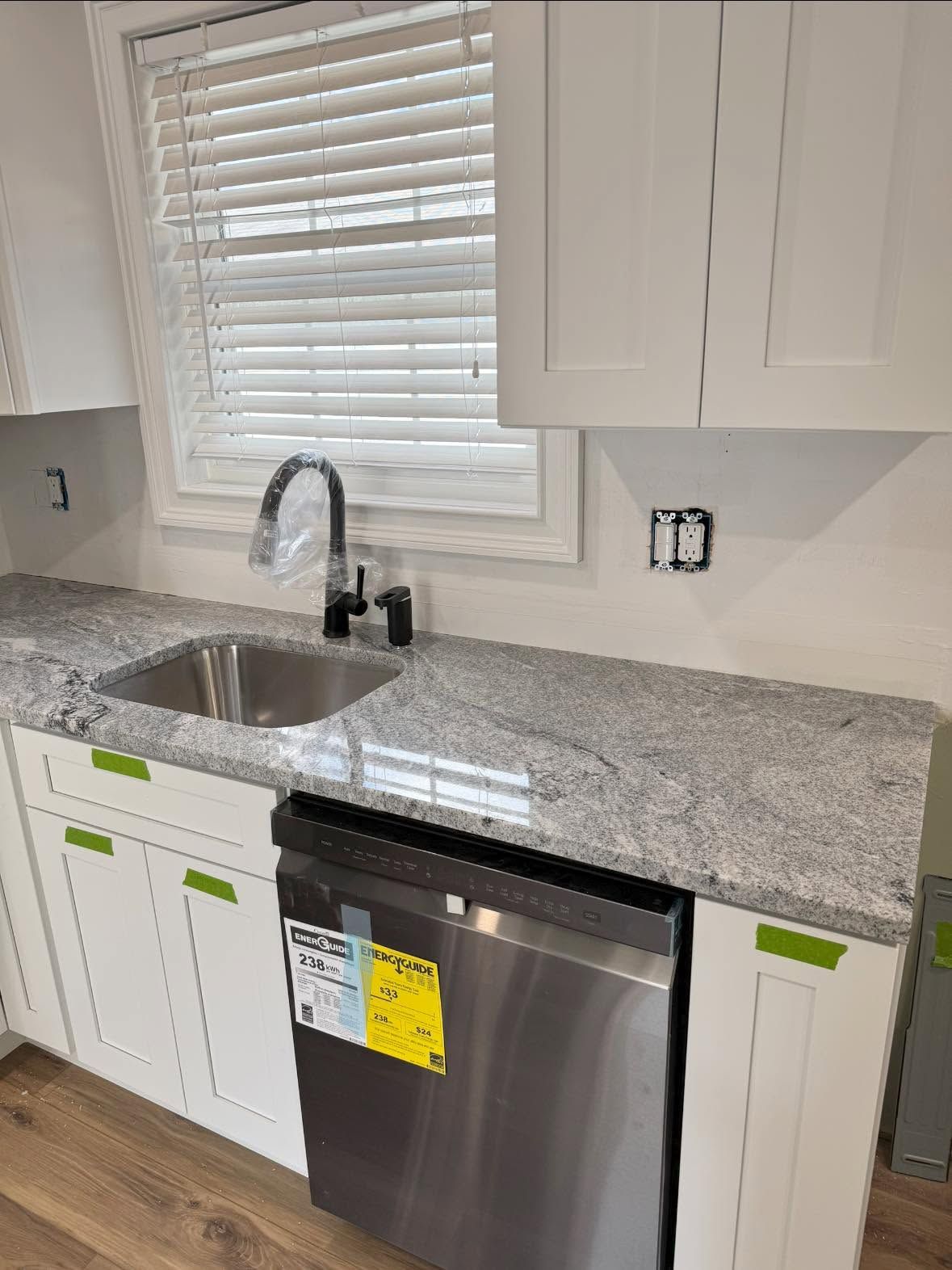 Modern kitchen sink with granite countertop, stainless faucet, white cabinets, and a stainless dishwasher