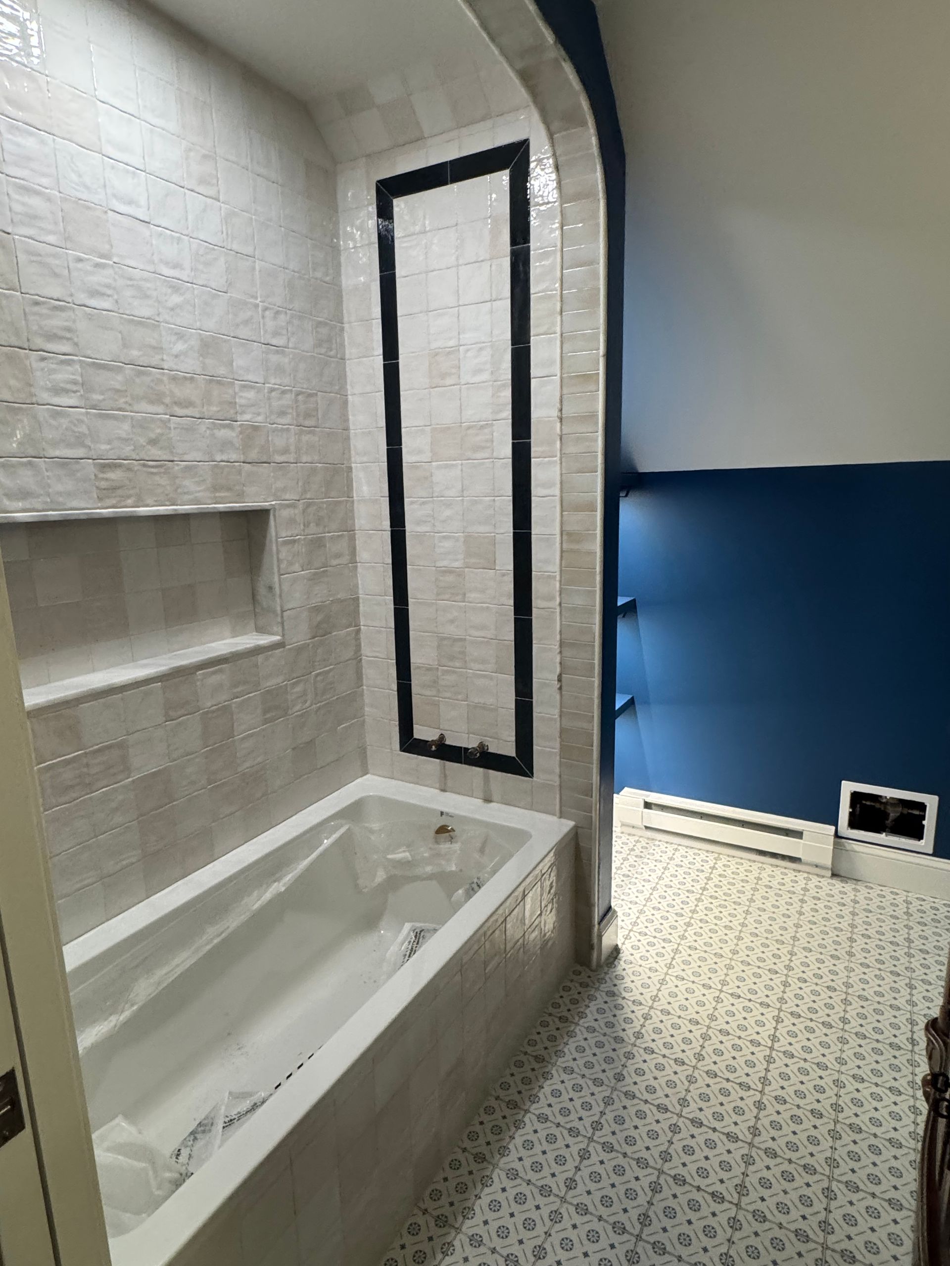 Small bathroom with white tub, tiled walls, dark-framed mirror, and blue accent wall.