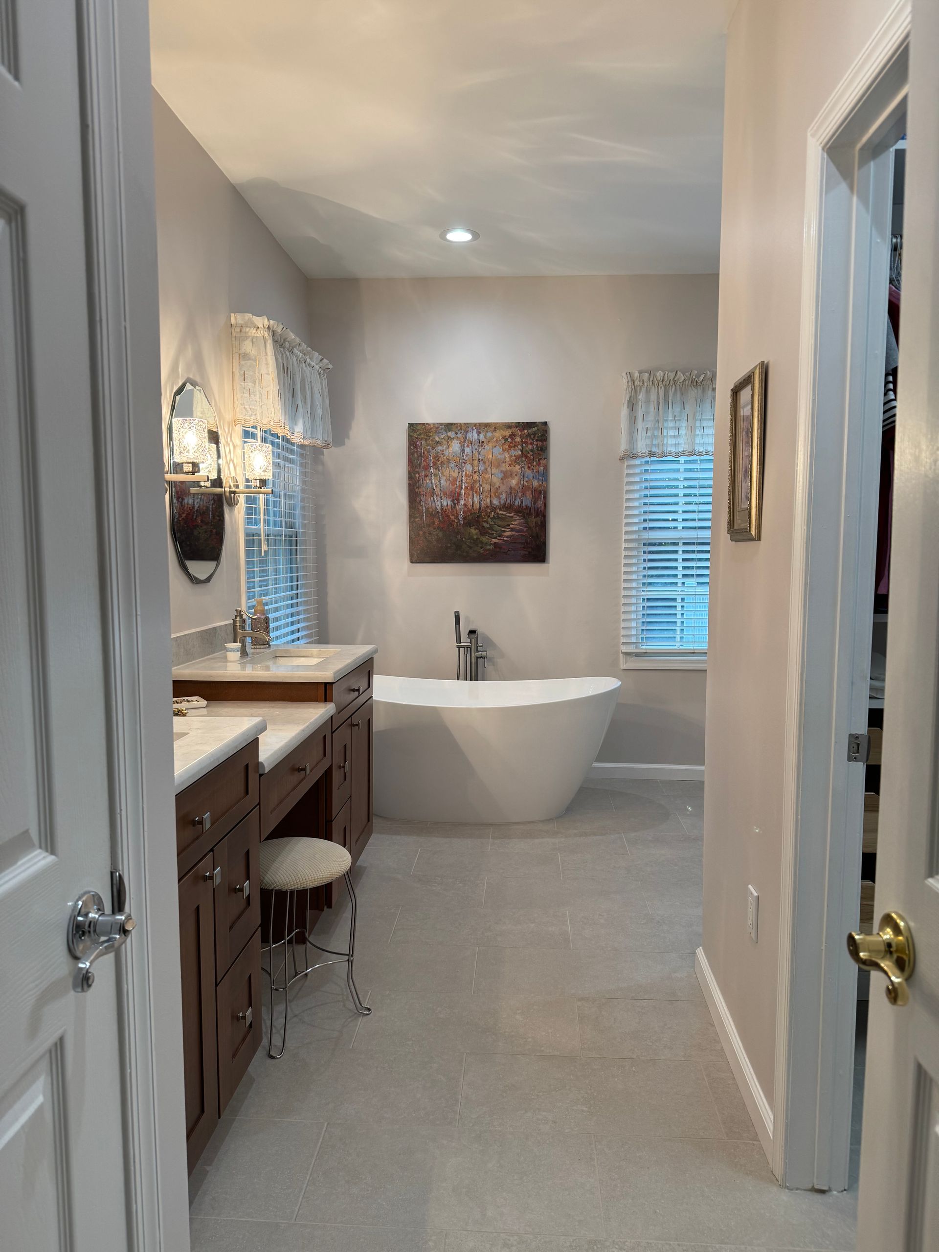 Bright bathroom with freestanding tub, double vanity, and windows with blinds.
