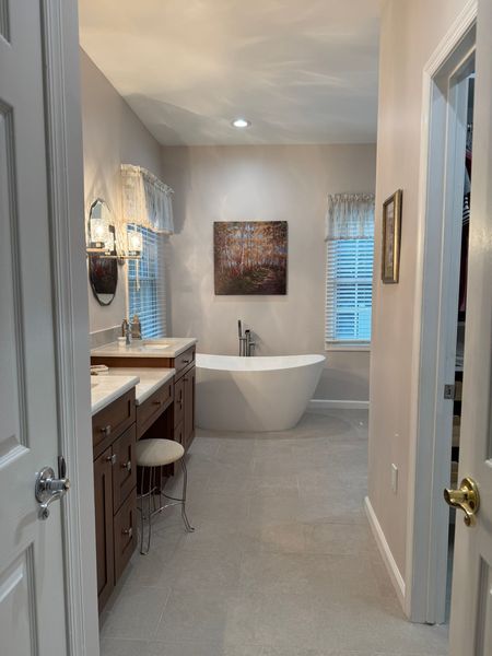 Modern bathroom with a freestanding tub, vanity, and two windows with blinds