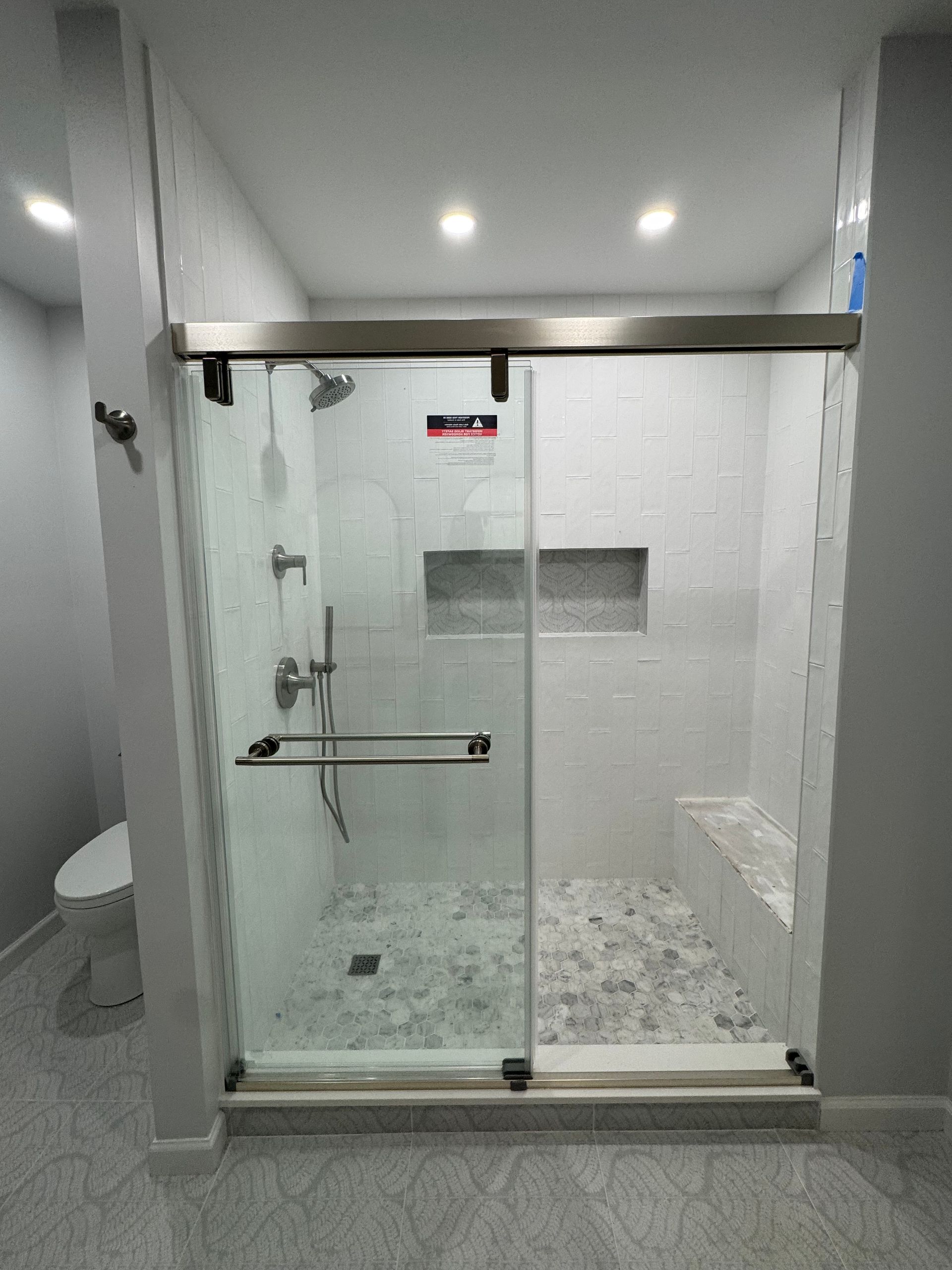 Modern glass shower enclosure with white tile walls and pebble floor in a bathroom