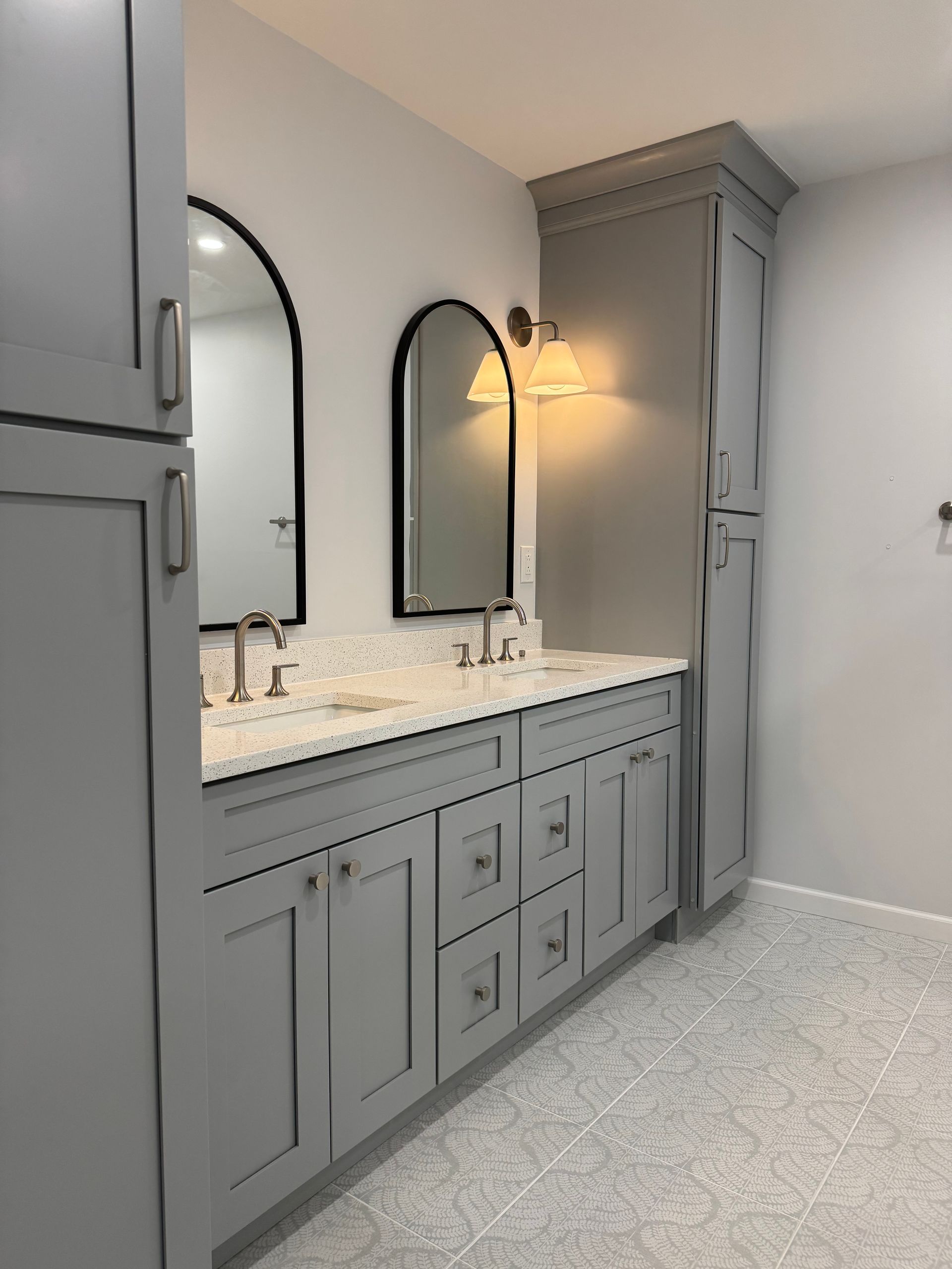 Gray bathroom vanity with marble countertop, arched mirrors, and wall sconces.