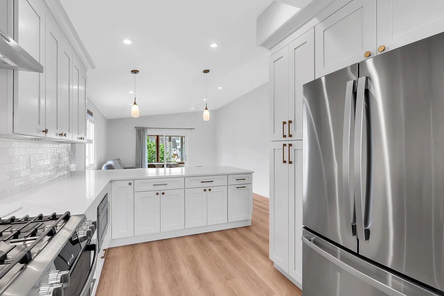 Bright modern white kitchen with stainless steel refrigerator and light wood floor