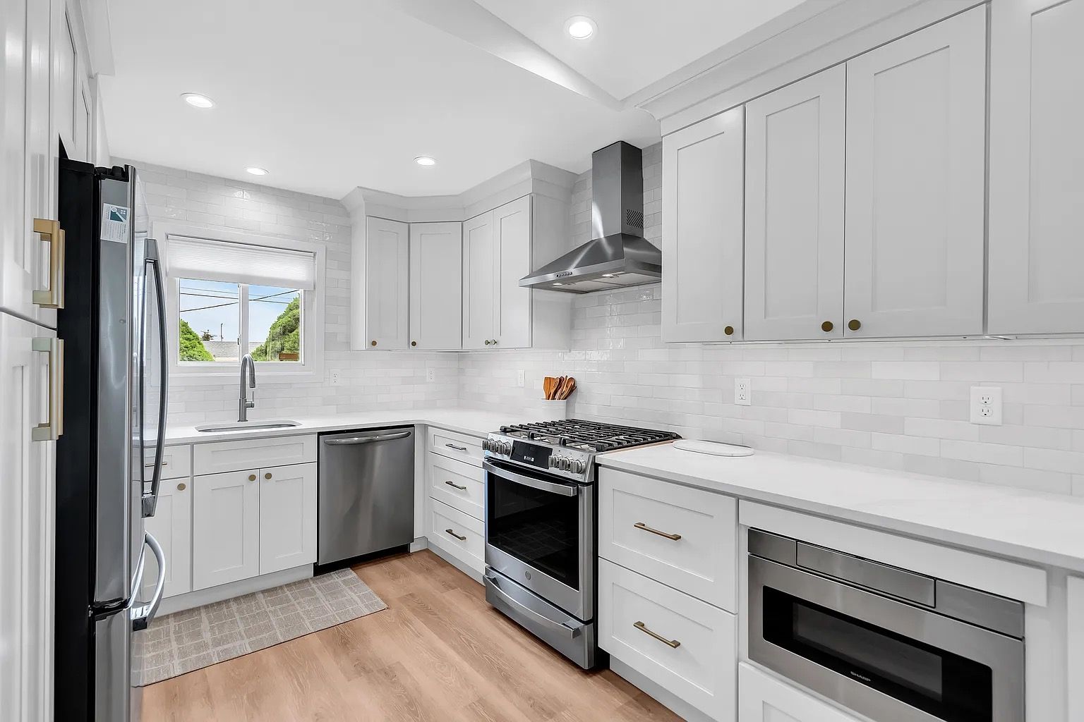 Bright white modern kitchen with stainless steel appliances, gray cabinets, and a window over the sink