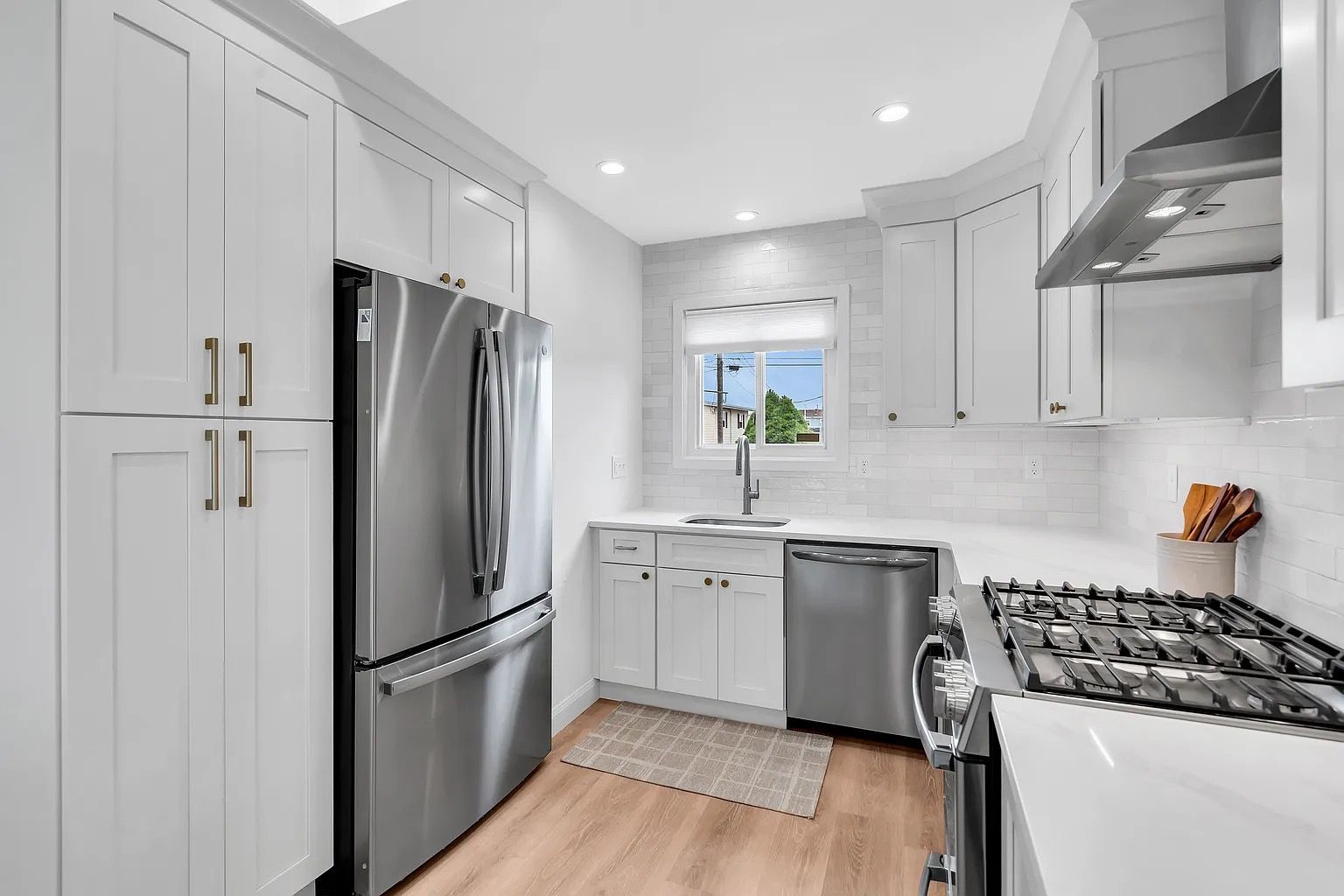 Bright modern kitchen with white cabinets, stainless steel appliances, and a small window above the sink.