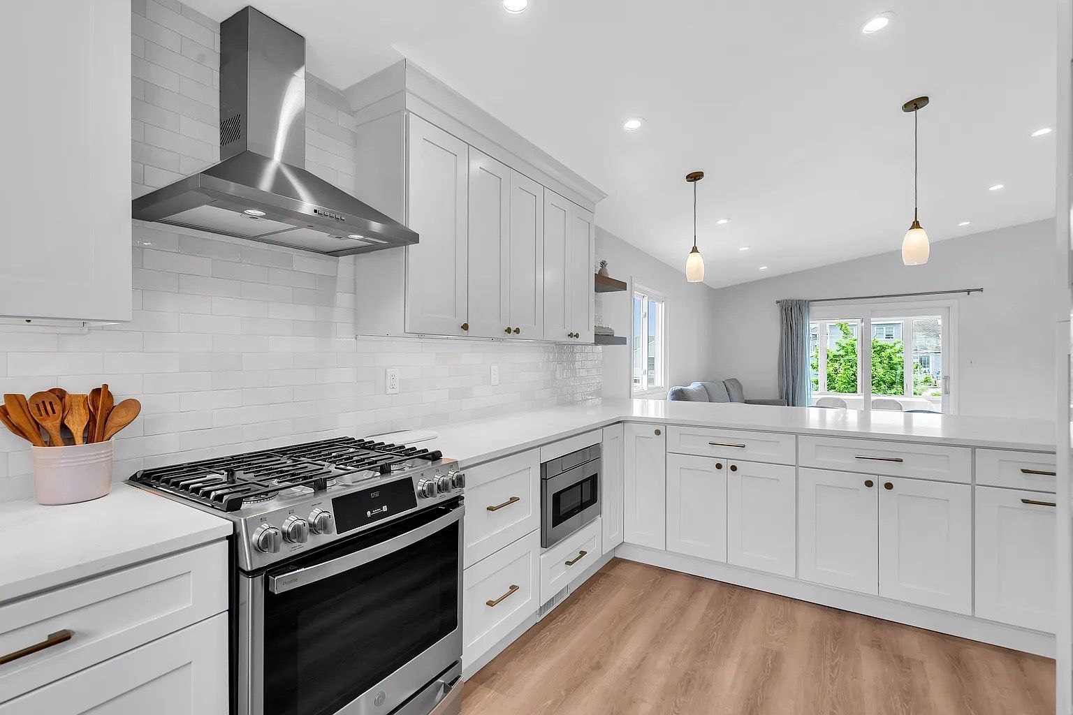 Bright white modern kitchen with stainless steel range, island, pendant lights, and wood floor