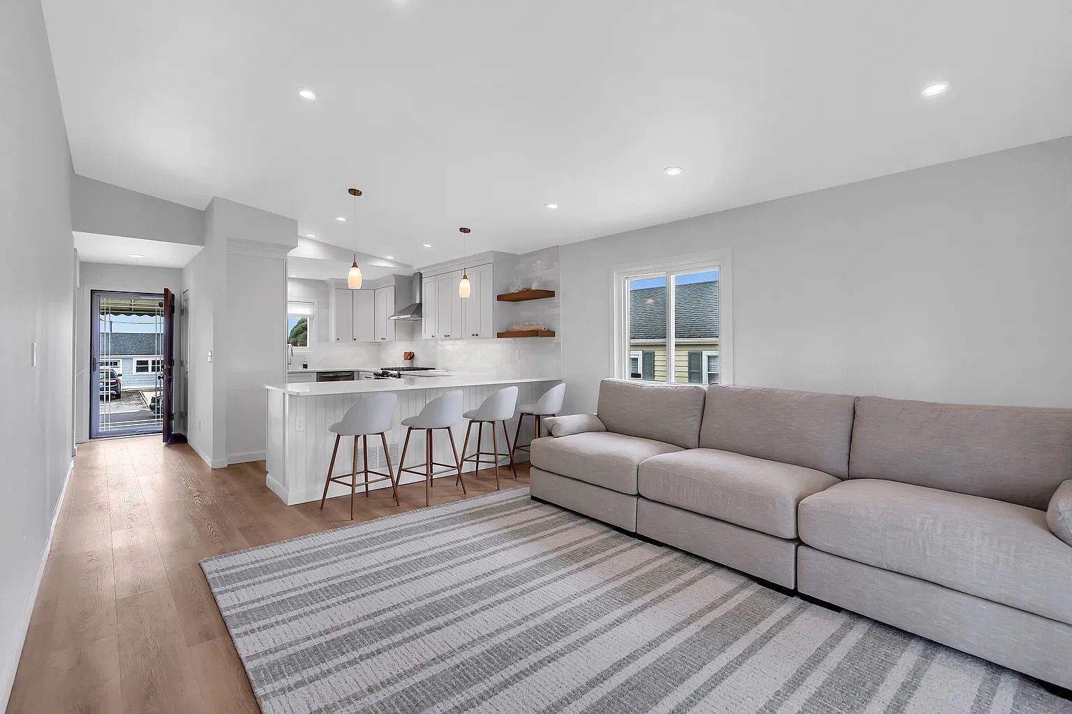 Bright open living room with gray sectional, striped rug, and kitchen island with stools