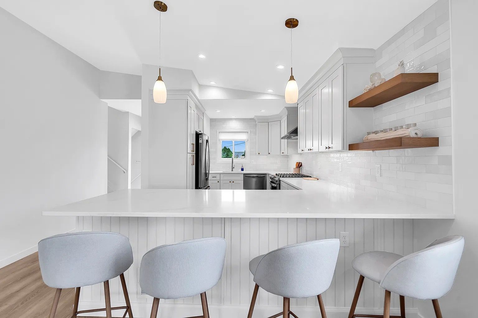 Bright white kitchen with marble island, pendant lights, and four light gray bar stools