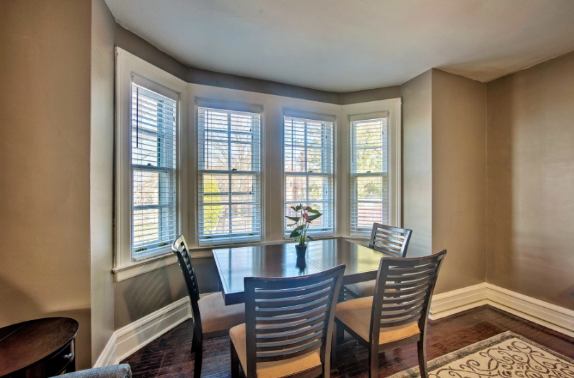 A dining room with a table and chairs in front of a bay window.