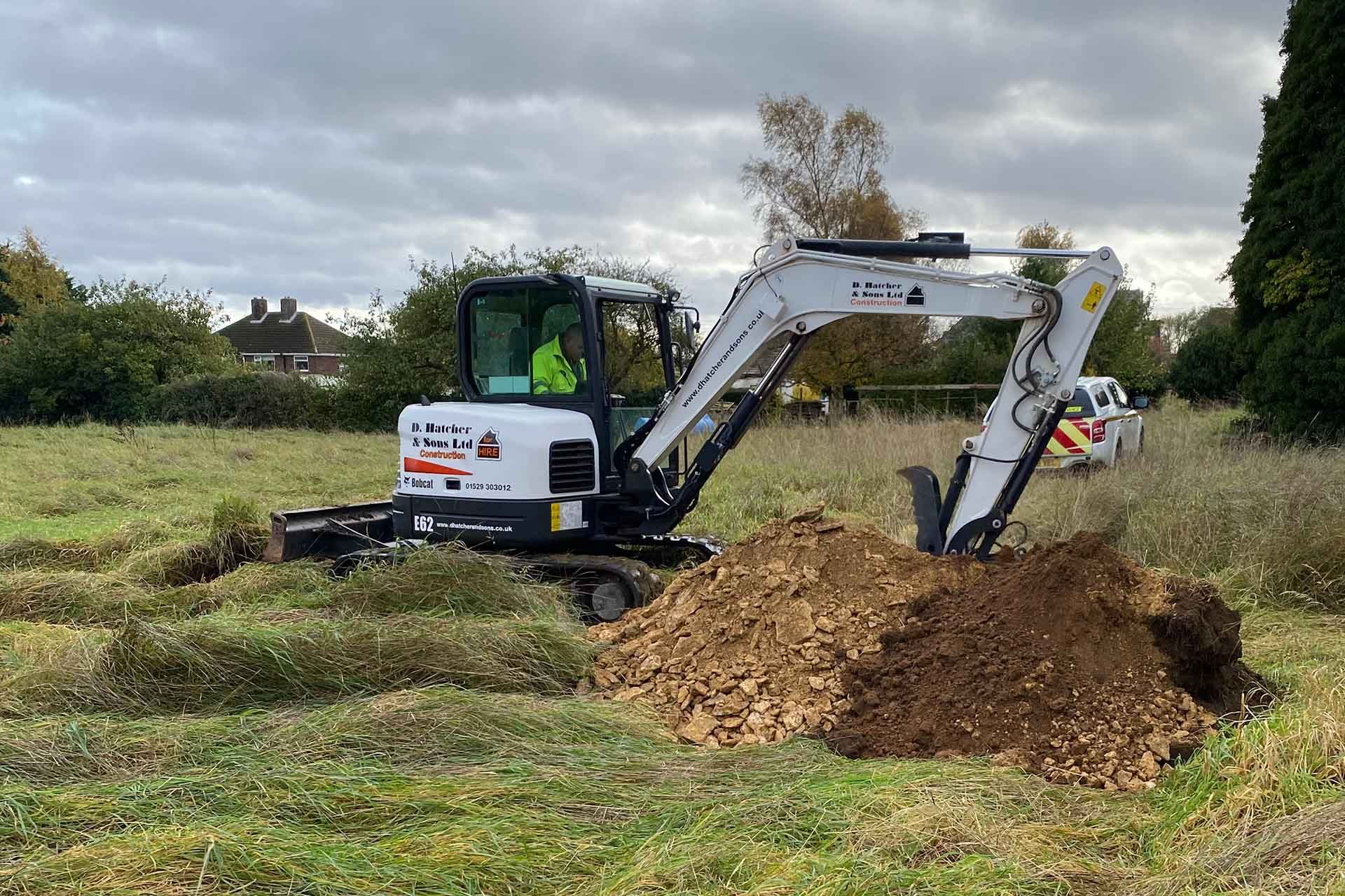 a DHS Plant Hire Bobcat mini excavator digging a hole in a field