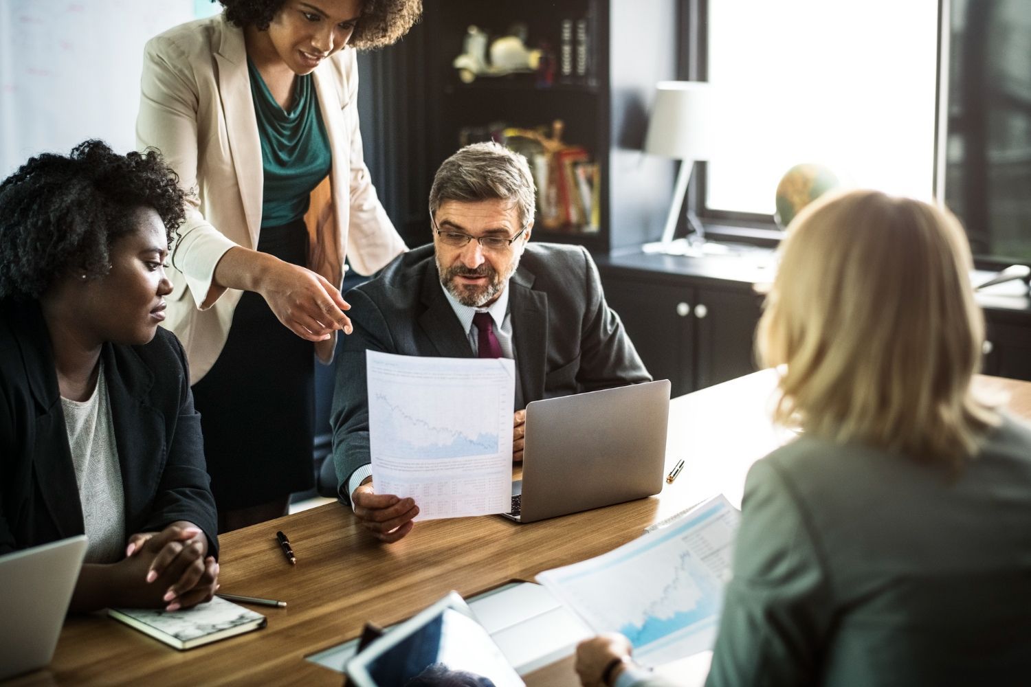 Business team at a wooden table reviewing charts; woman pointing, laptop open. Corporation/LLC Issues Law Attorney in Nashville, Tennessee