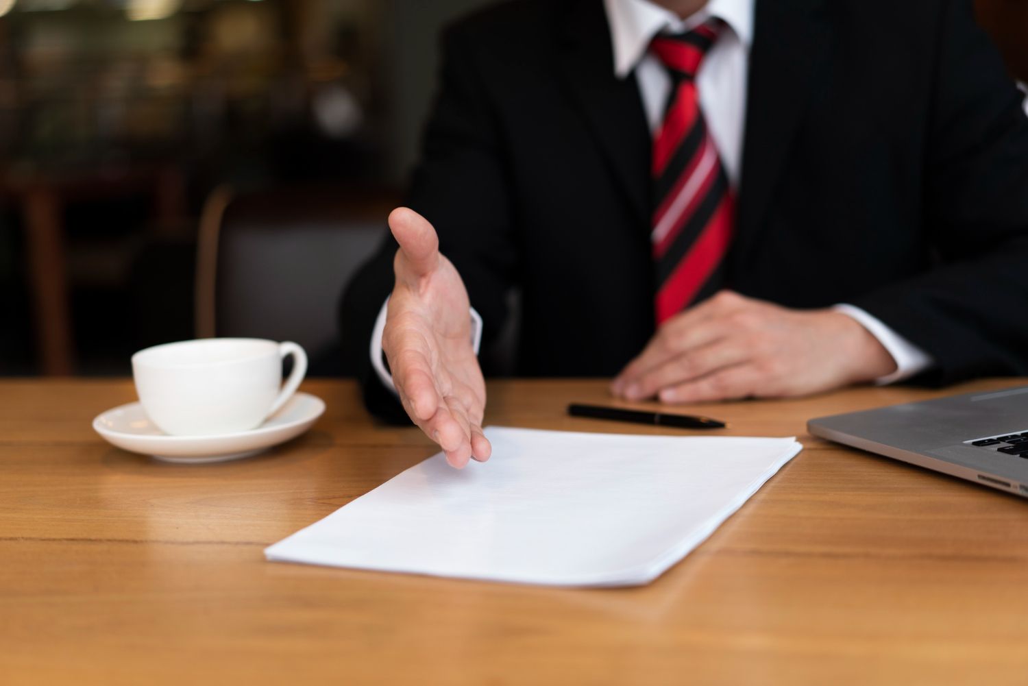 Person in suit extends hand over a blank document on a wooden table. Breach of Contract Law Attorney in Nashville, Tennessee