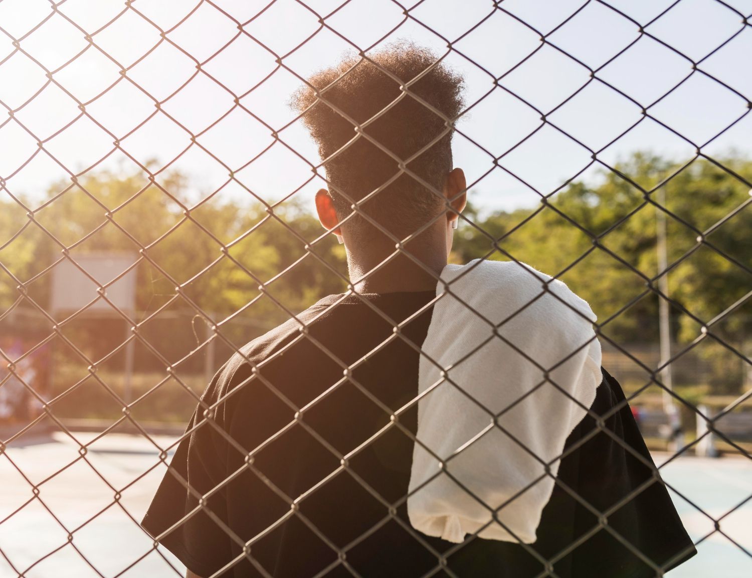 Person standing behind chain-link fence, white towel on shoulder, looking away. Juvenile Defense Law Attorney in Nashville, Tennessee