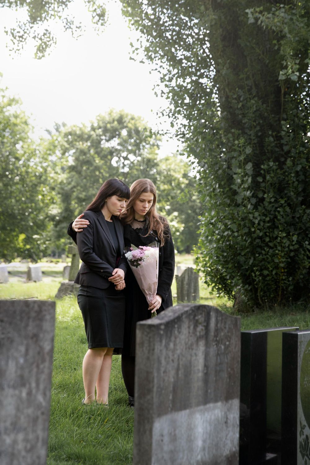 Two women at a gravesite; one with arm around the other, holding flowers, expressing grief. Wrongful Death Law Attorney in Nashville, Tennessee
