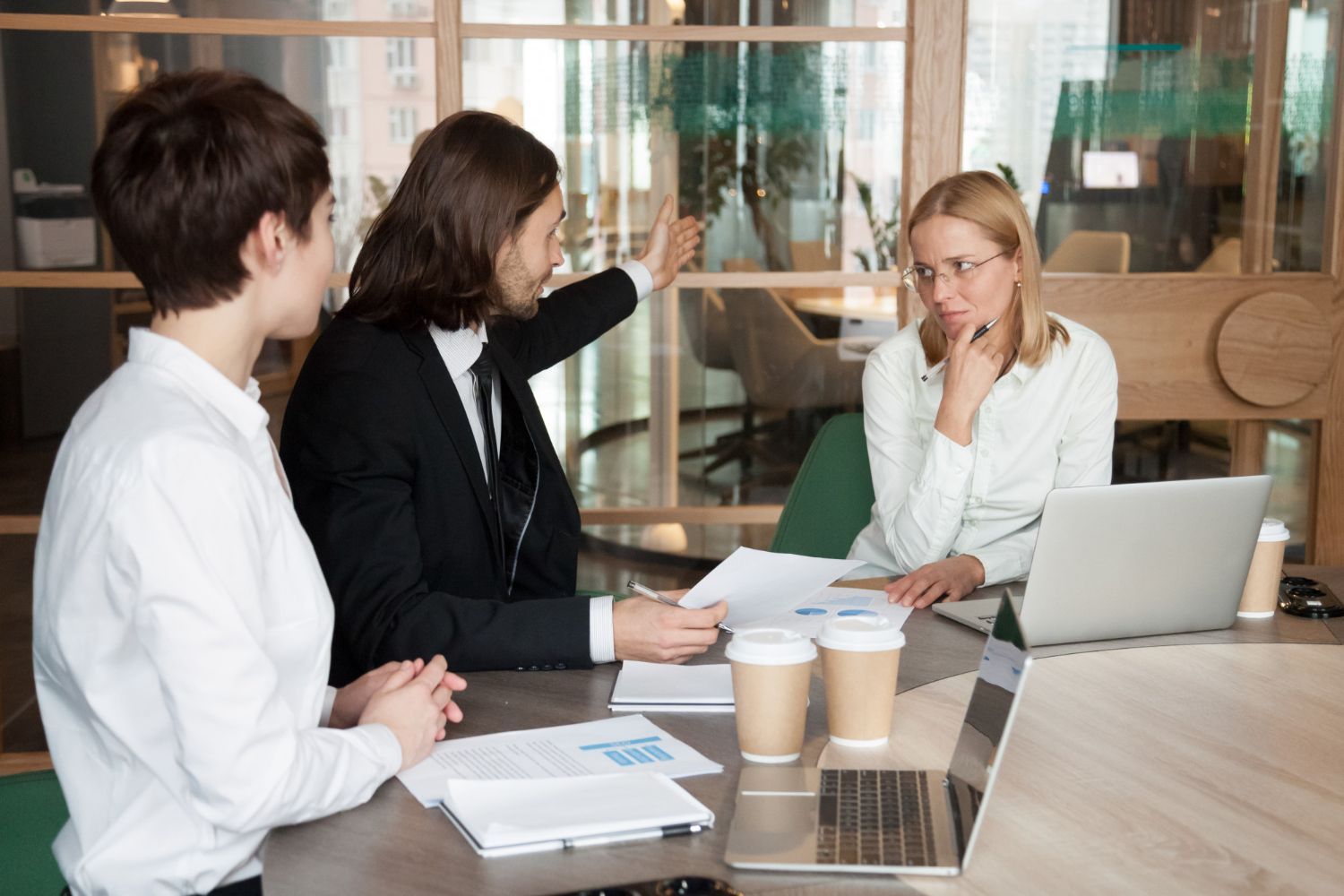 Three people in a business meeting. A man gestures at papers, looking frustrated; two women look on, one thoughtful. Commercial Disputes Law Attorney in Nashville, Tennessee