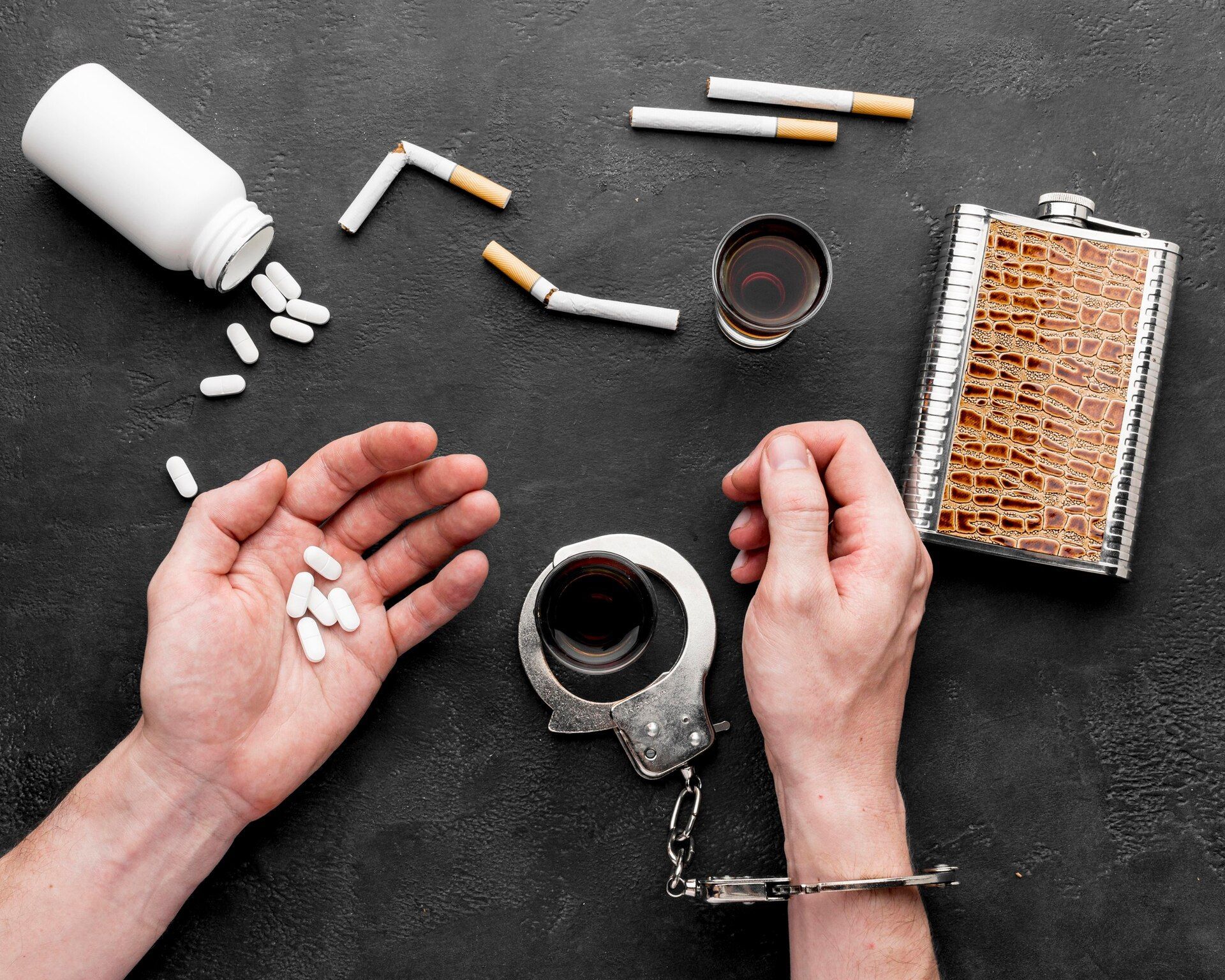 Hands with pills and handcuffed over liquor glass, cigarettes, alcohol flask, and spilled pills. Drug Offenses Law Attorney in Nashville, Tennessee