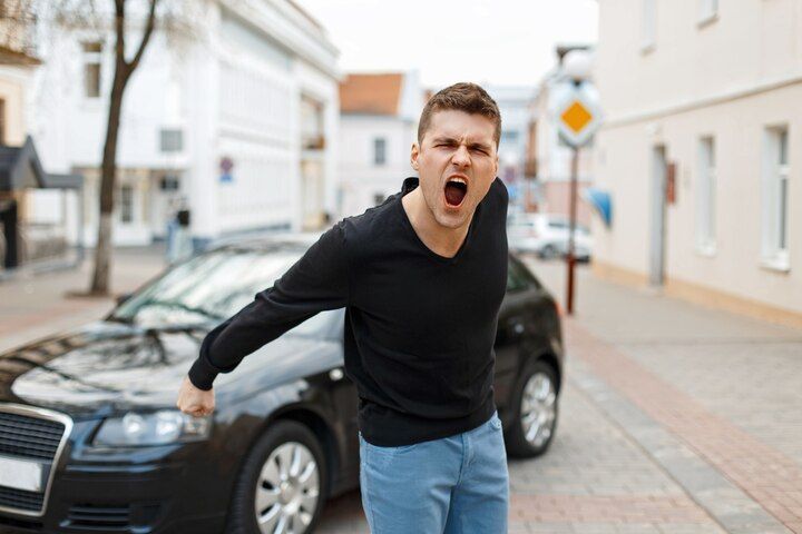 Man yelling next to black car on city street. He wears black top and blue jeans, with angry expression. Hit and Run Law Attorney in Nashville, Tennessee