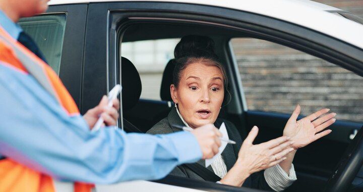 Woman in car looking surprised, gesturing with hands; person in orange vest outside car. Traffic Violations / CDL Law Attorney in Nashville, Tennessee