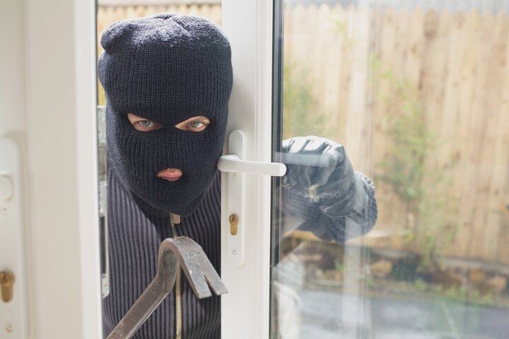 Person in a black ski mask using a crowbar to open a glass door. Aggravated Burglary Law Attorney in Nashville Tennessee