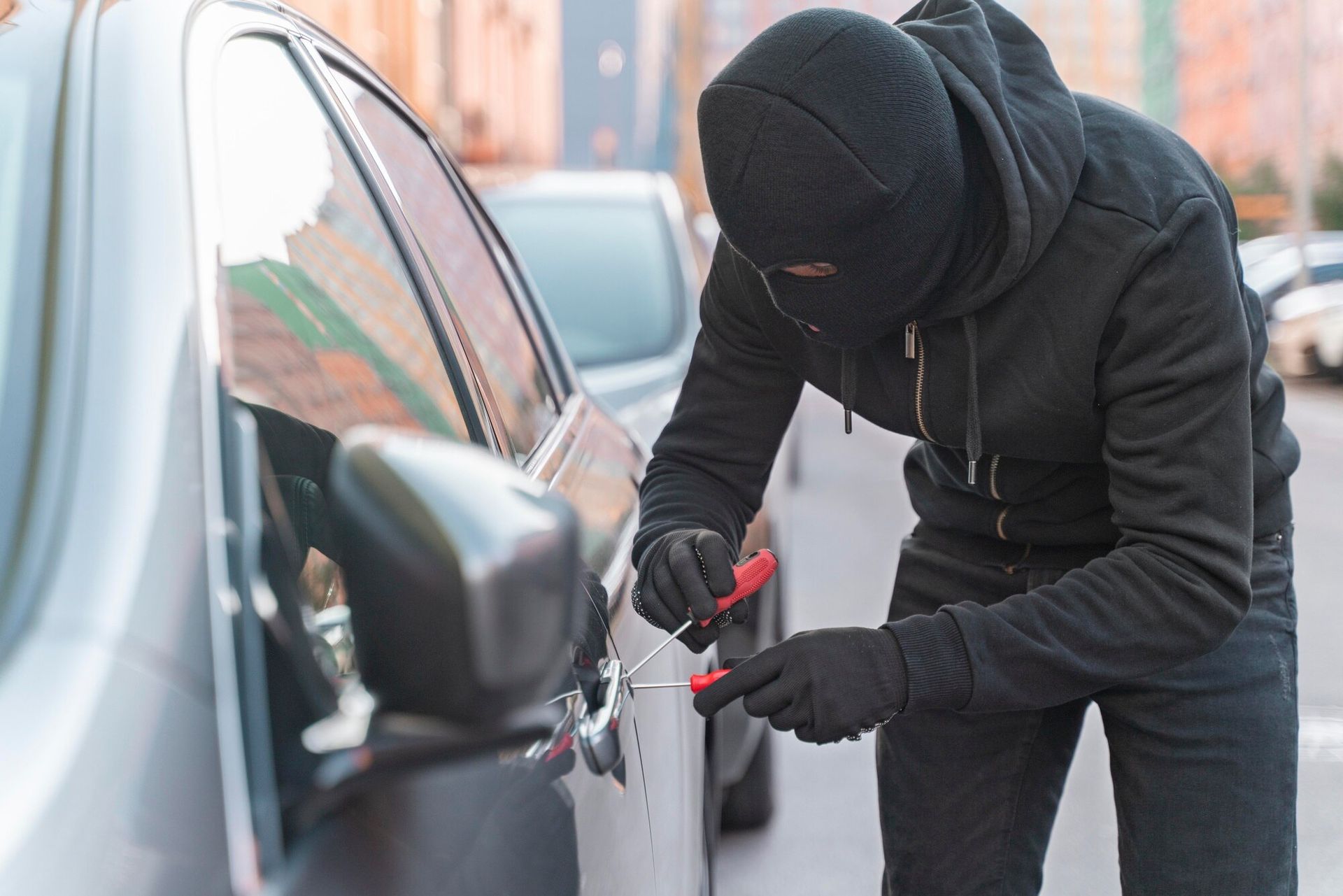 Person in black clothing and balaclava using tools to open a car door. Carjacking Law Attorney in Nashville, Tennessee