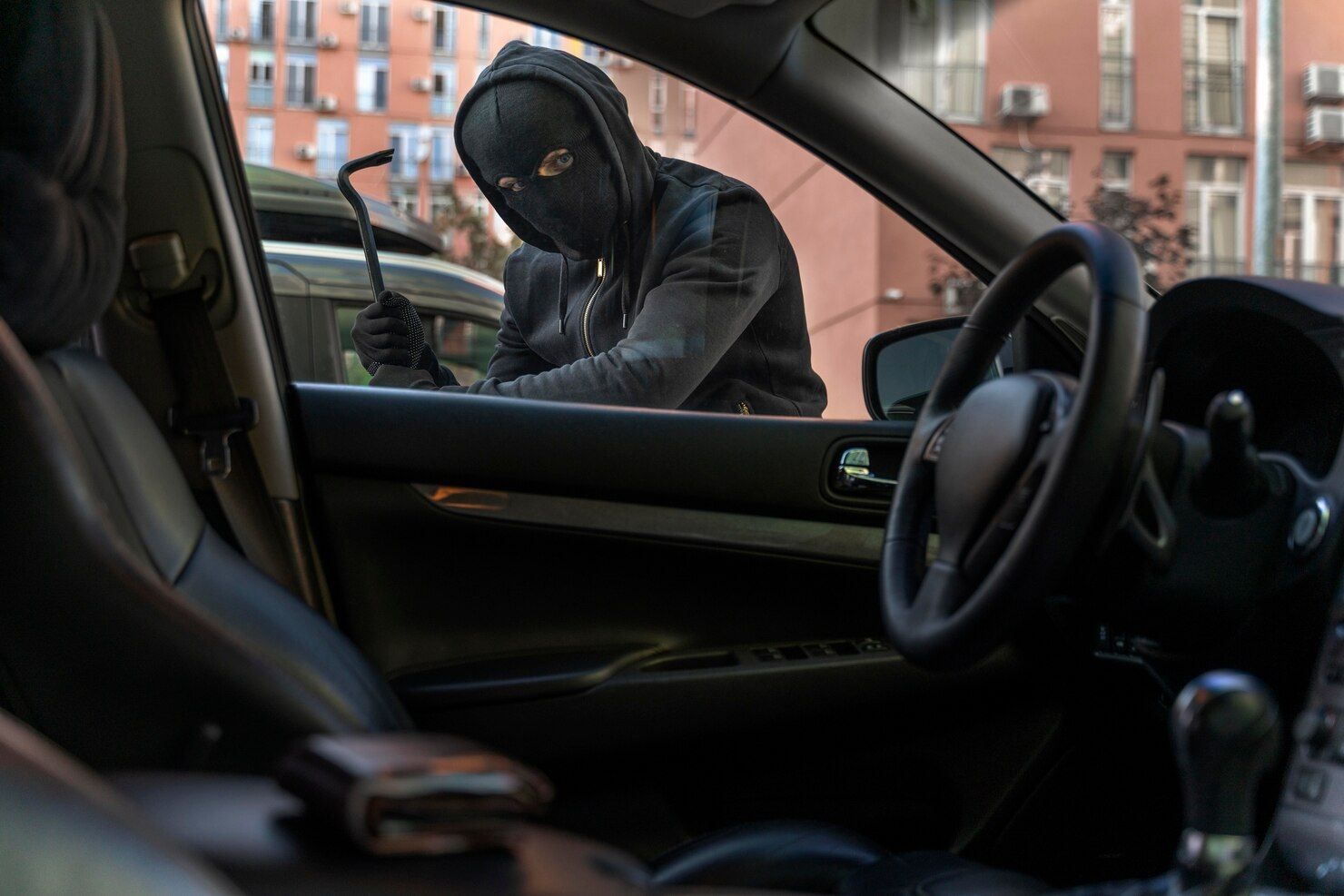 A masked person using a crowbar to break into a car, viewed from inside the vehicle. Robbery Law Attorney in Nashville, Tennessee