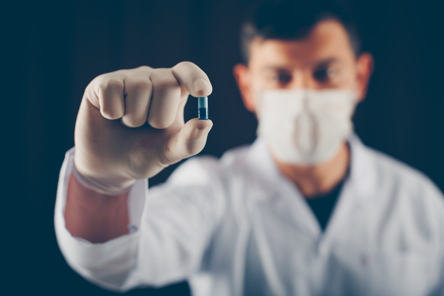Person in lab coat and mask holding a blue capsule between gloved fingers. Drug Conspiracy Law Attorney in Nashville, Tennessee