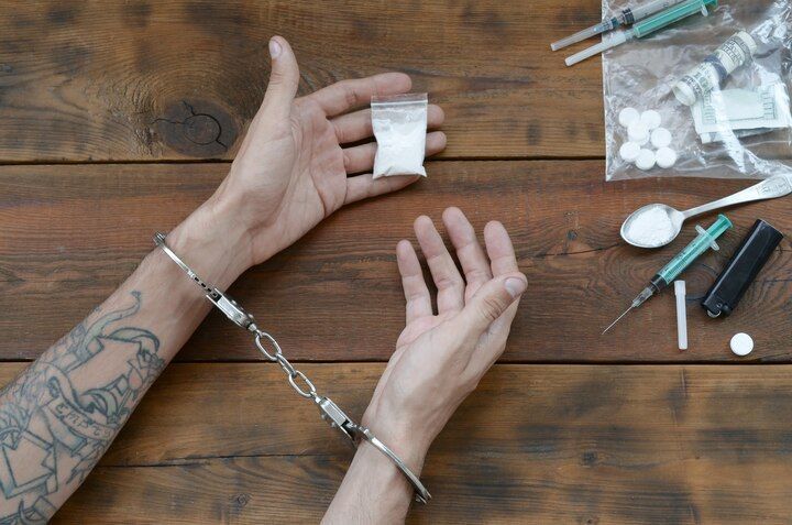 Hands cuffed on a wooden surface, holding a bag of white powder, with drug paraphernalia nearby. Drug Possession Law Attorney in Nashville, Tennessee