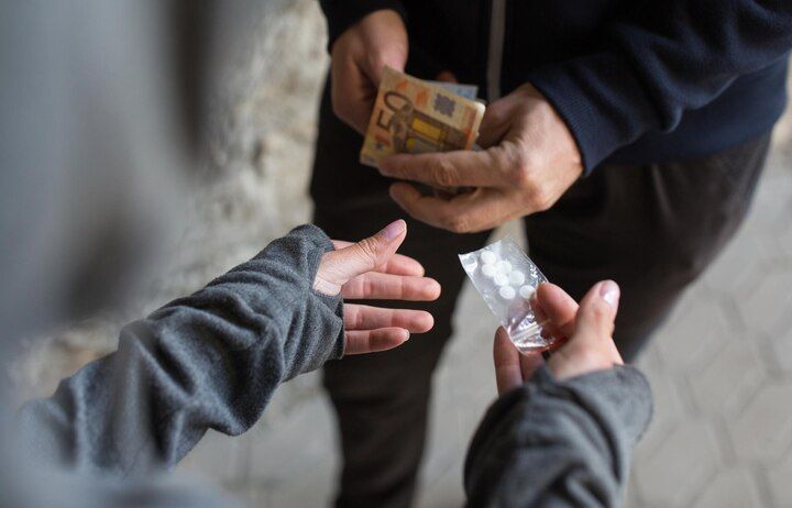 Hands exchanging money and small bag of pills; drug deal. Drug Sale & Delivery Law Attorney in Nashville, Tennessee