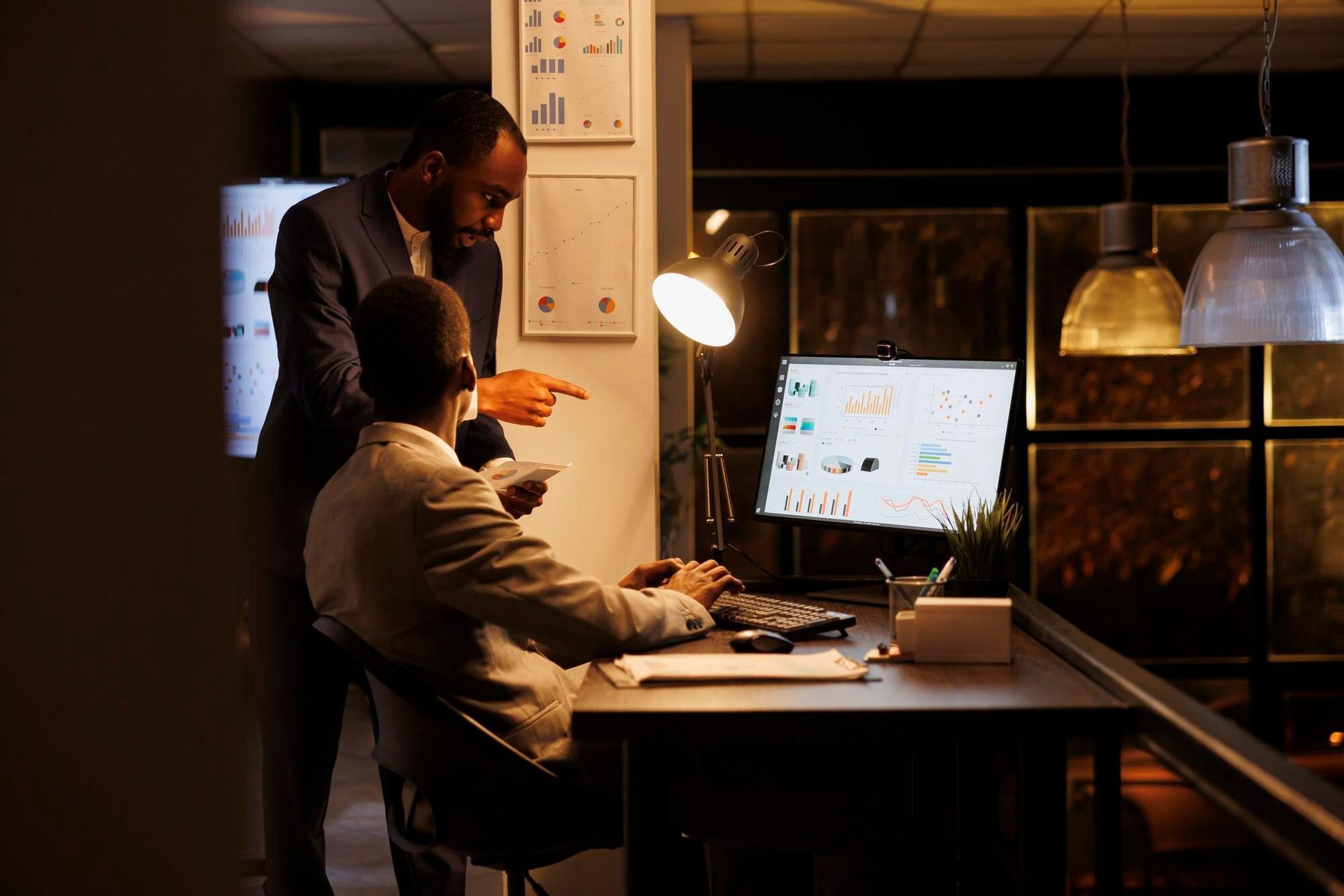 Two people reviewing computer screen data in dimly lit office. One points while the other types. Criminal Simulation Law Attorney in Nashville, Tennessee