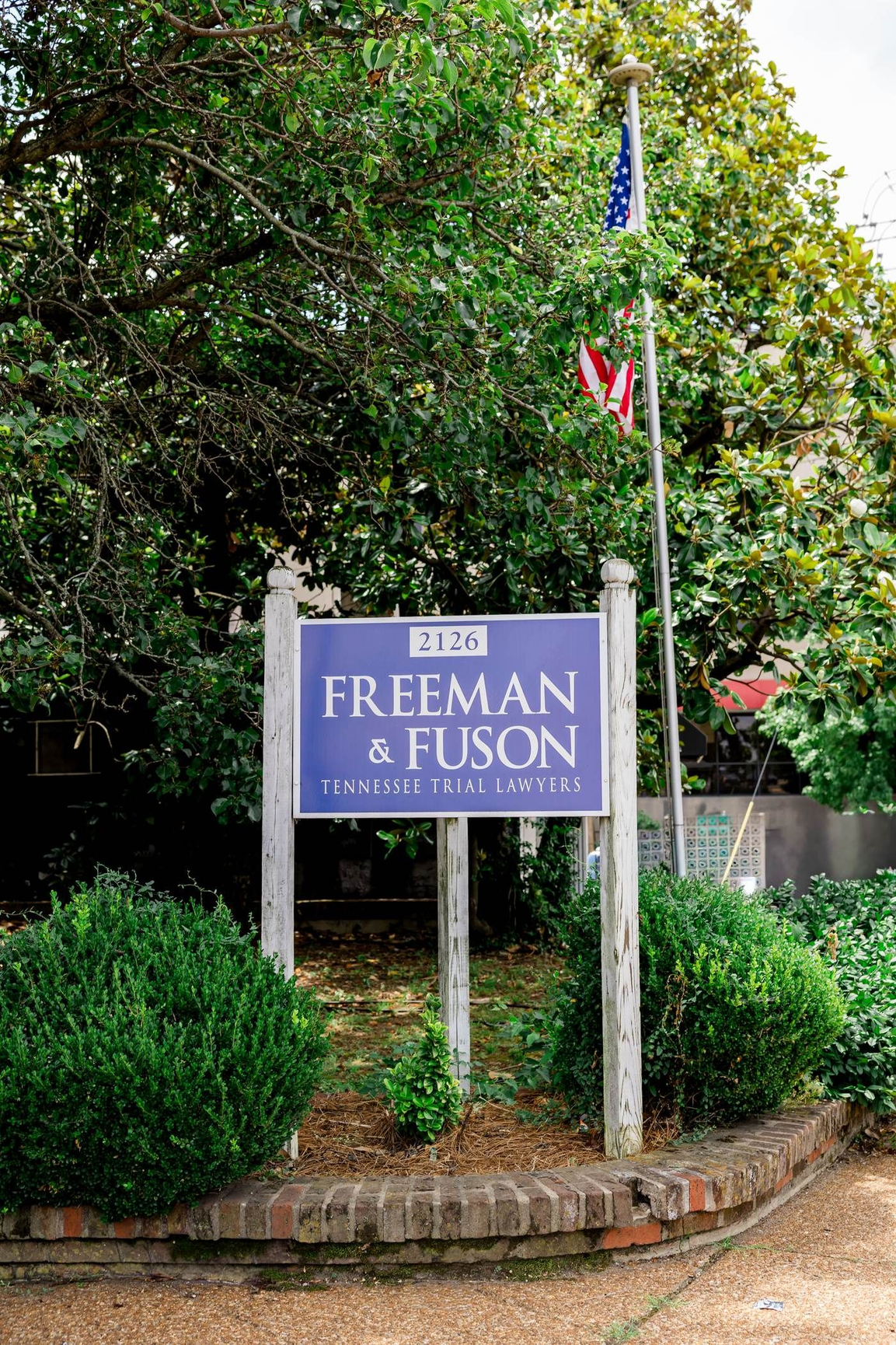 Sign for Freeman & Fuson, a legal firm. Blue sign with white lettering and an arrow. Over a doorway, beneath autumn foliage. Freeman & Fuson Trial Lawyers in Nashville, Tennessee