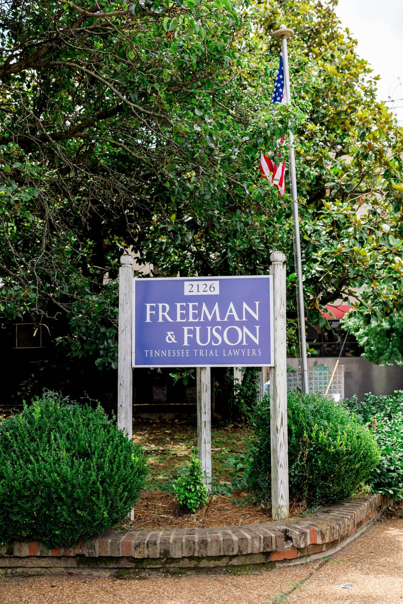 Sign for Freeman & Fuson, a legal firm. Blue sign with white lettering and an arrow. Over a doorway, beneath autumn foliage. Freeman & Fuson Trial Lawyers in Nashville, Tennessee