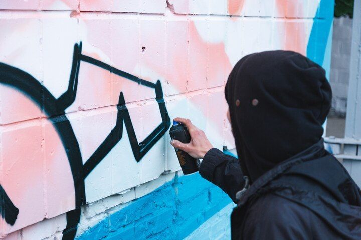 Person in black hoodie spray-painting graffiti on a brick wall, using black paint. Vandalism Law Attorney in Nashville Tennessee