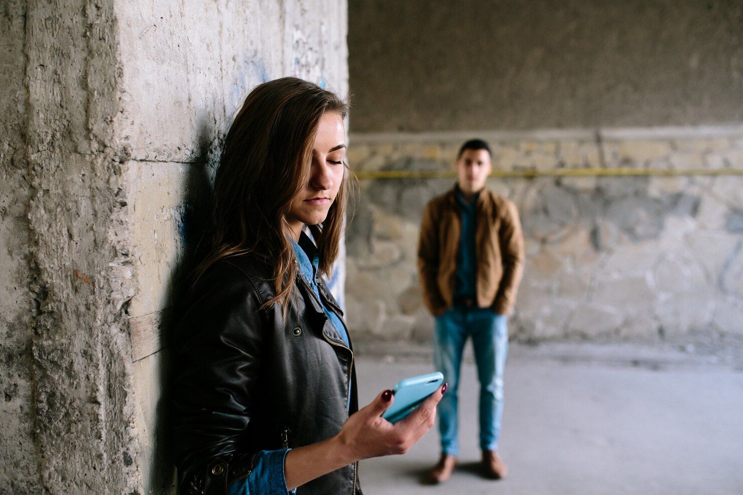 Woman using phone leaning against a concrete wall, man stands in the background.  Stalking Law Attorney in Nashville, Tennessee