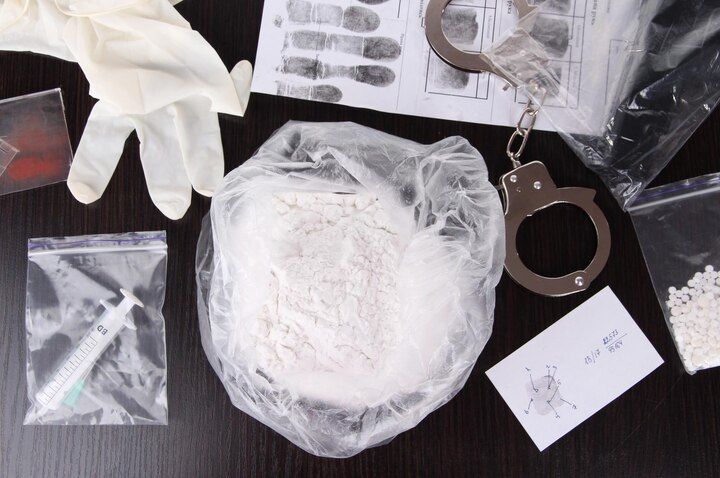 Evidence: bag of powder, syringe, handcuffs, fingerprints, gloves, small bags on a table. Drug Manufacturing Law Attorney in Nashville, Tennessee