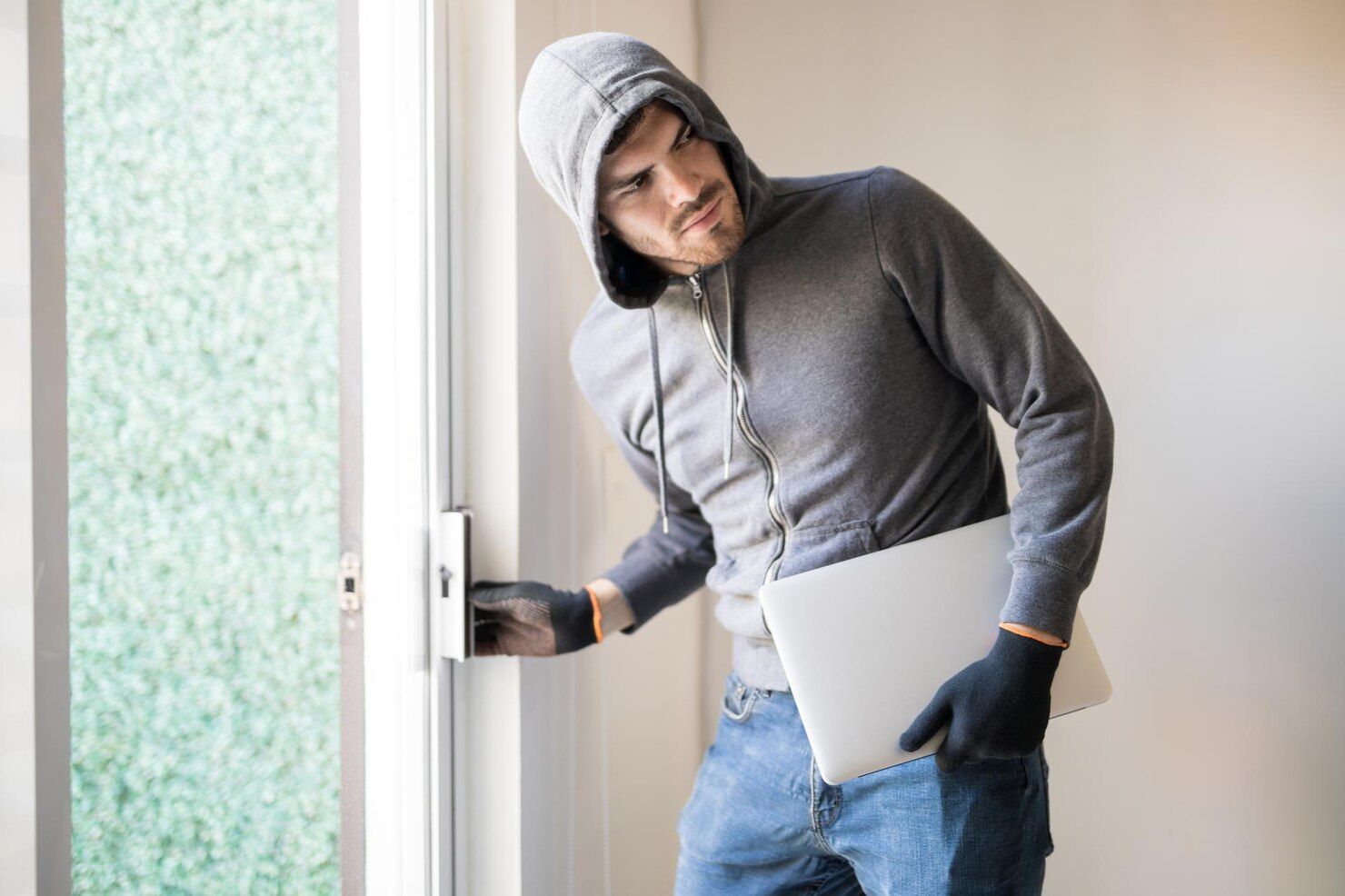 Person in a hoody and gloves opens a door while holding a laptop. Burglary Law Attorney at Freeman & Fuson in Nashville, Tennessee