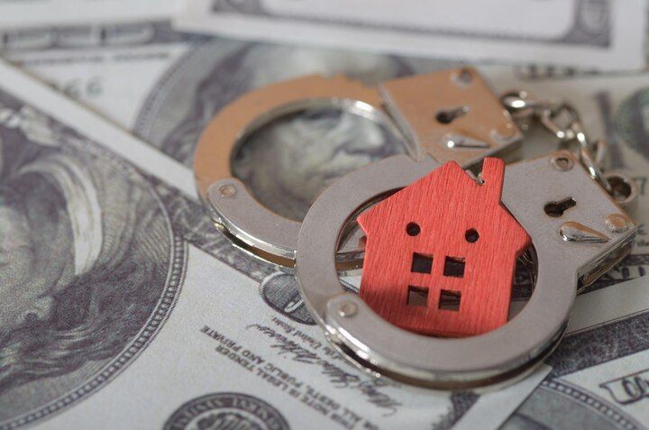 Handcuffs around a red house model on a bed of US dollar bills. Property Crimes Law Attorney in Nashville, Tennessee