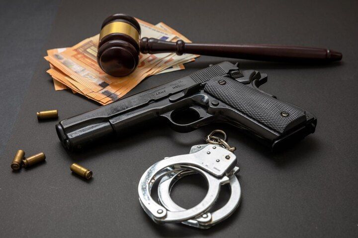 Handgun, handcuffs, gavel, and cash on a dark surface. Unlawful Weapon Possession Law Attorney in Nashville, Tennessee