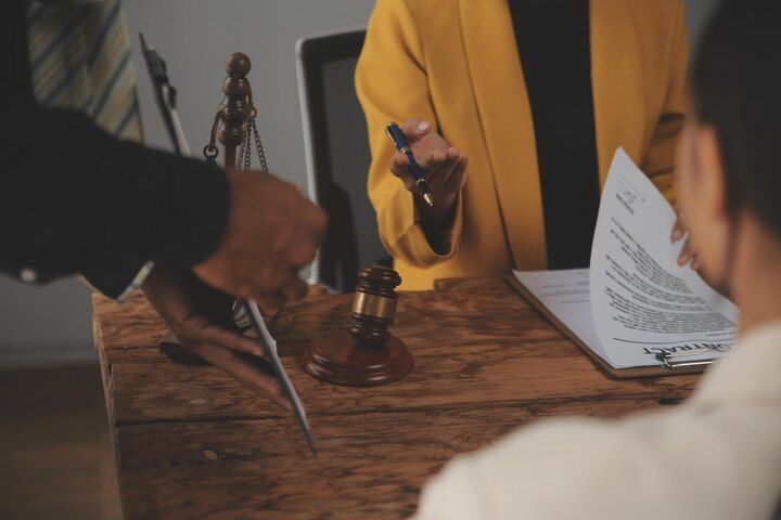 Lawyers at a wooden desk with a gavel, legal documents, and a client signing papers. Disorderly Conduct Law Attorney in Nashville, Tennessee
