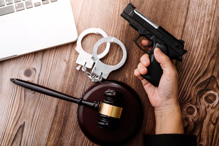 Hand holding a handgun, handcuffs, gavel, and laptop on a wooden surface. Weapons Charges Law Attorney in Nashville, Tennessee