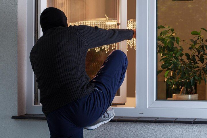 Person in a dark sweater and balaclava climbing through a window at night. Criminal Trespass in Nashville, Tennessee