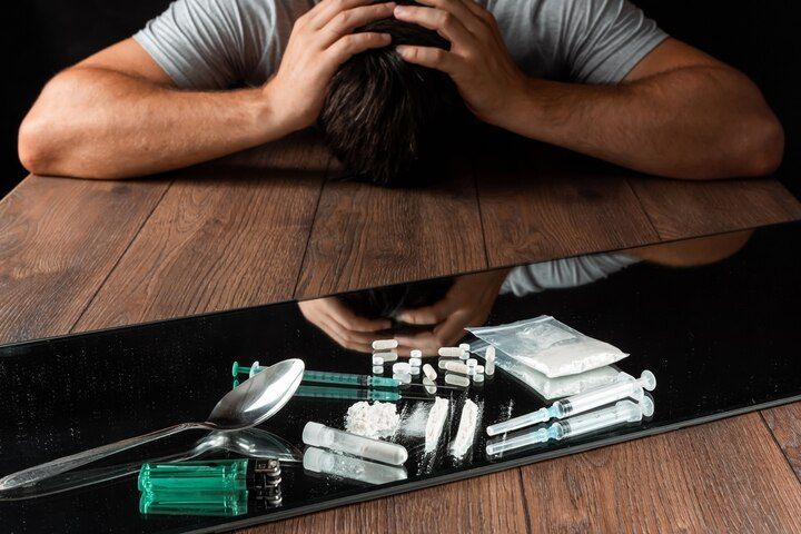 Man with head in hands above drugs, syringes, and a spoon on a reflective surface. Drug Possession Law Attorney in Nashville, Tennessee