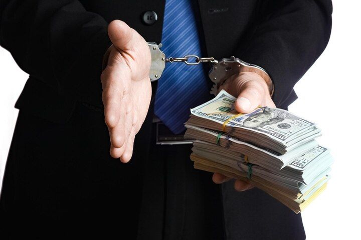 Person in suit handcuffed, offering handshake with one hand and stacks of cash with the other. White Collar & Financial Crimes Law Attorney in Nashville, Tennessee