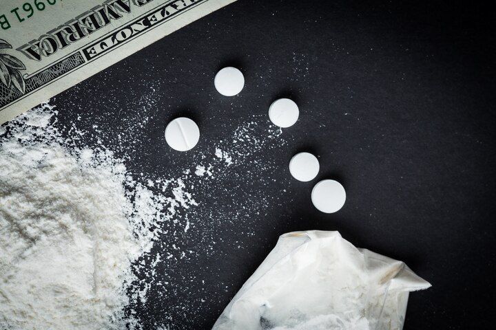 Pills, white powder, and money on a black surface, suggesting illicit drug use and financial transaction. Drug Conspiracy Law Attorney in Nashville, Tennessee